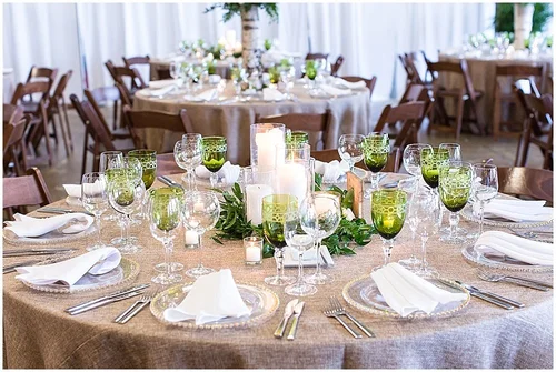 Round reception tables with green glassware, pillar candles and low greenery runners