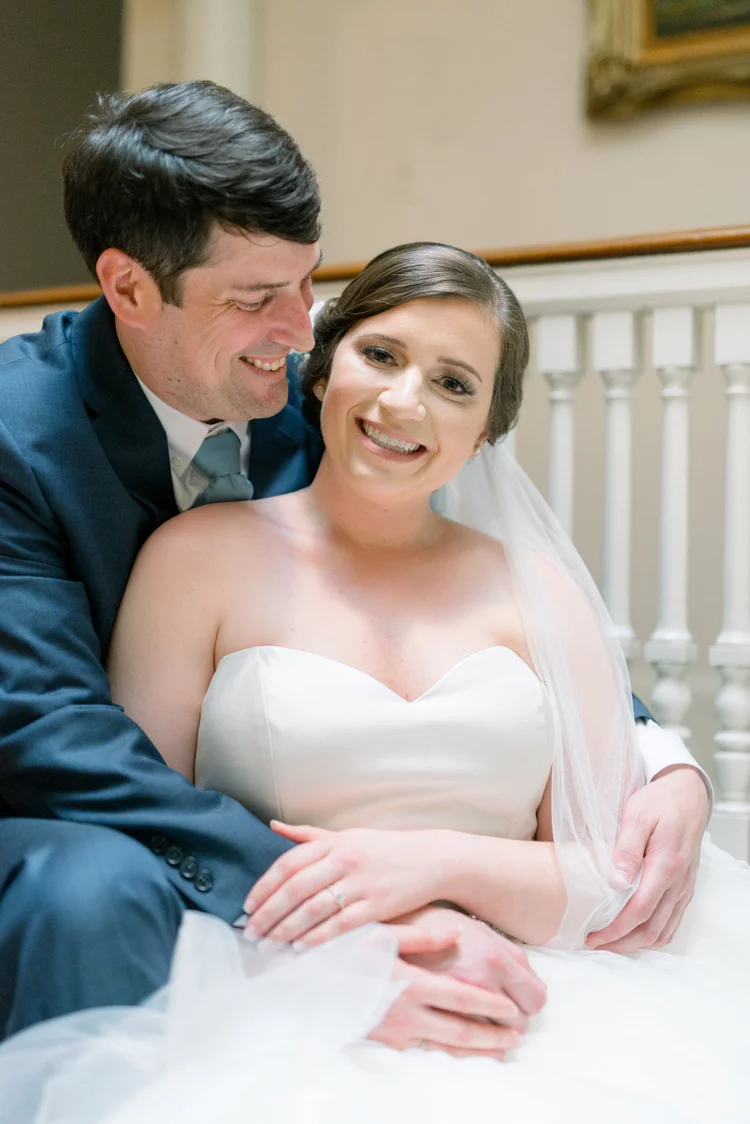 Groom in a blue suit resting his head against a smiling bride in a strapless gown