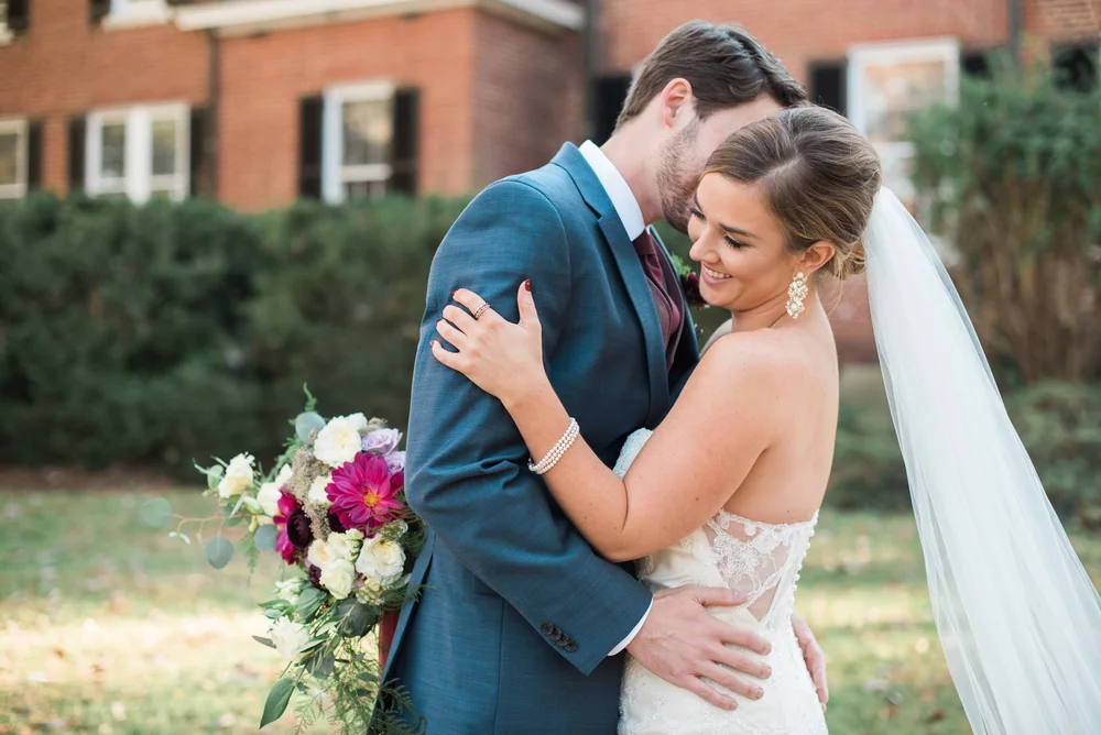 Bride with a jewel-toned bouquet resting against a groom in a teal blue suit