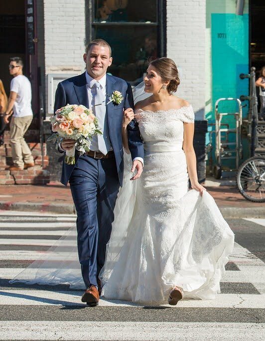 Bride holding her train and groom with a bouquet crossing a crosswalk downtown