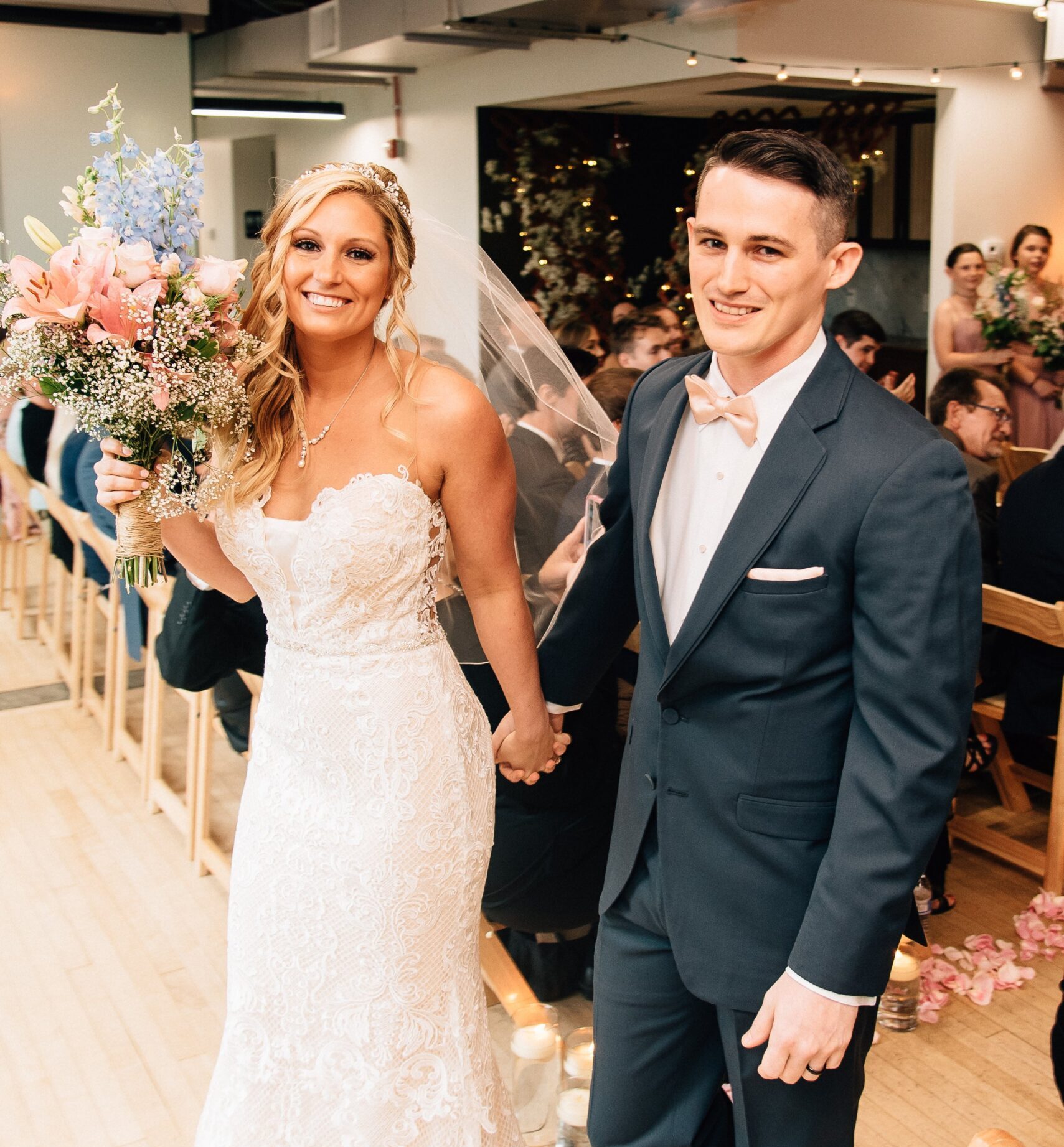 Bride holding a blush bouquet beside the groom in a charcoal suit indoors