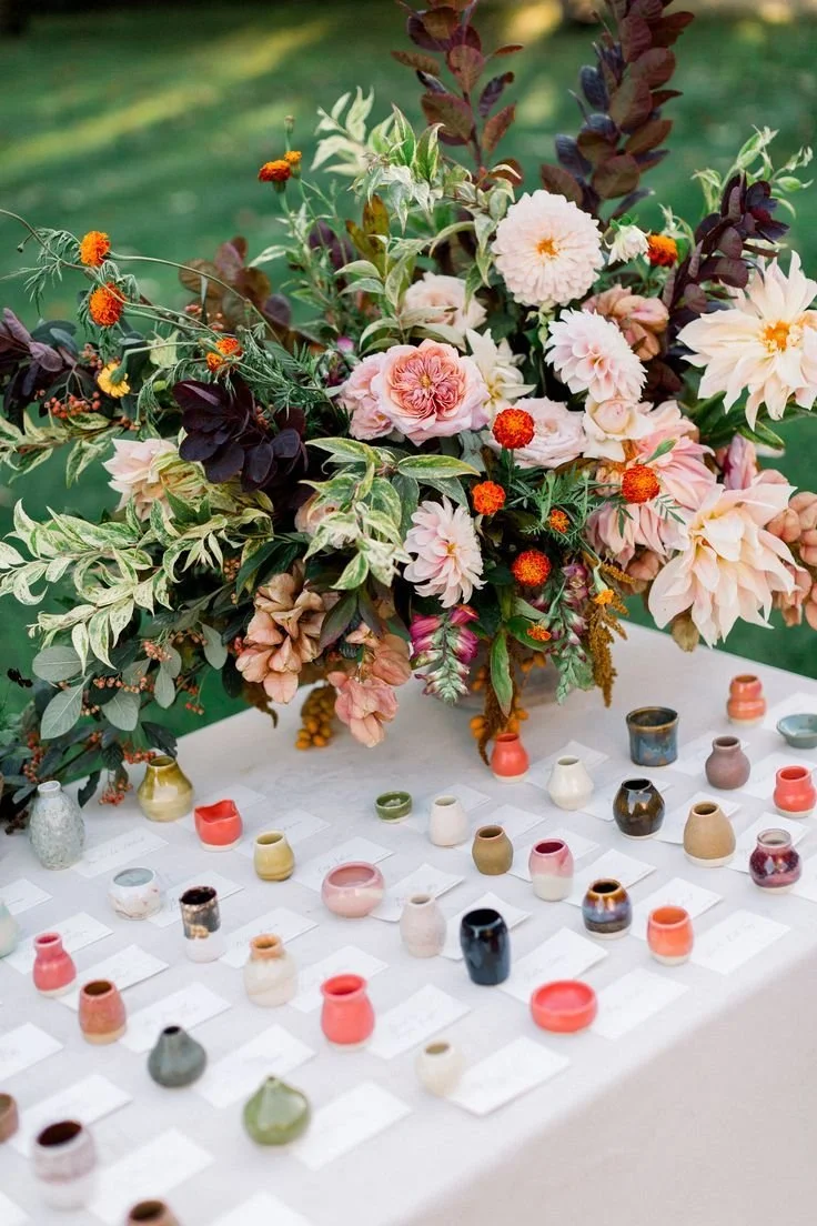 Lush floral arrangement above a row of small handmade glazed pottery favours