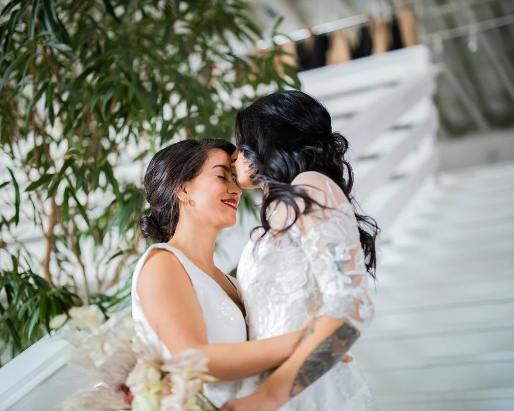 Two brides embracing under greenery