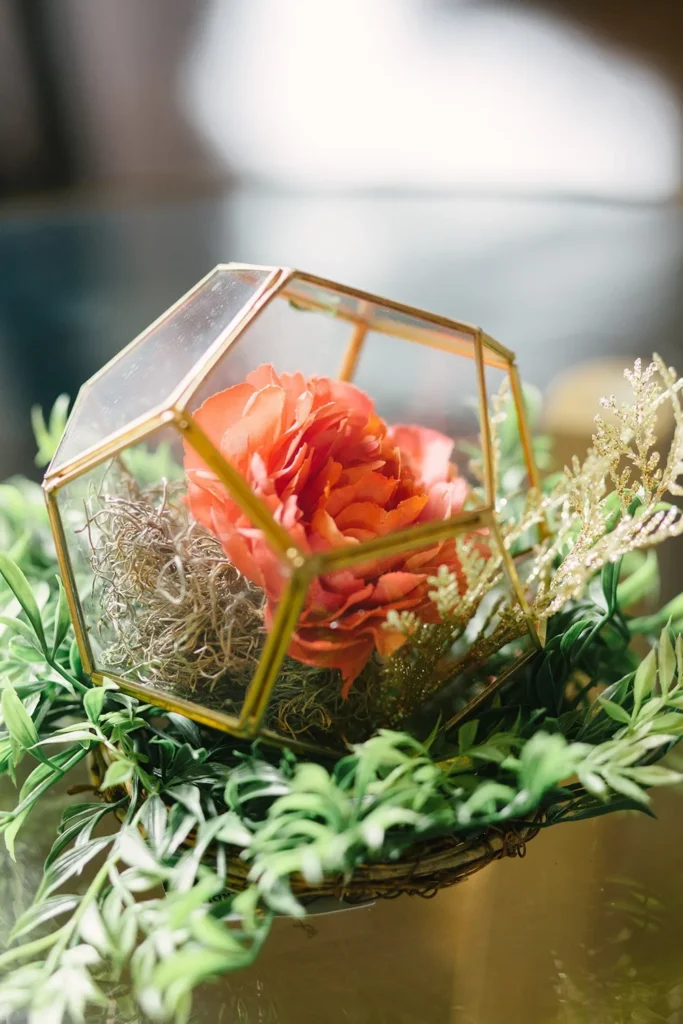 Gold geometric glass terrarium holding coral peonies and moss among greenery