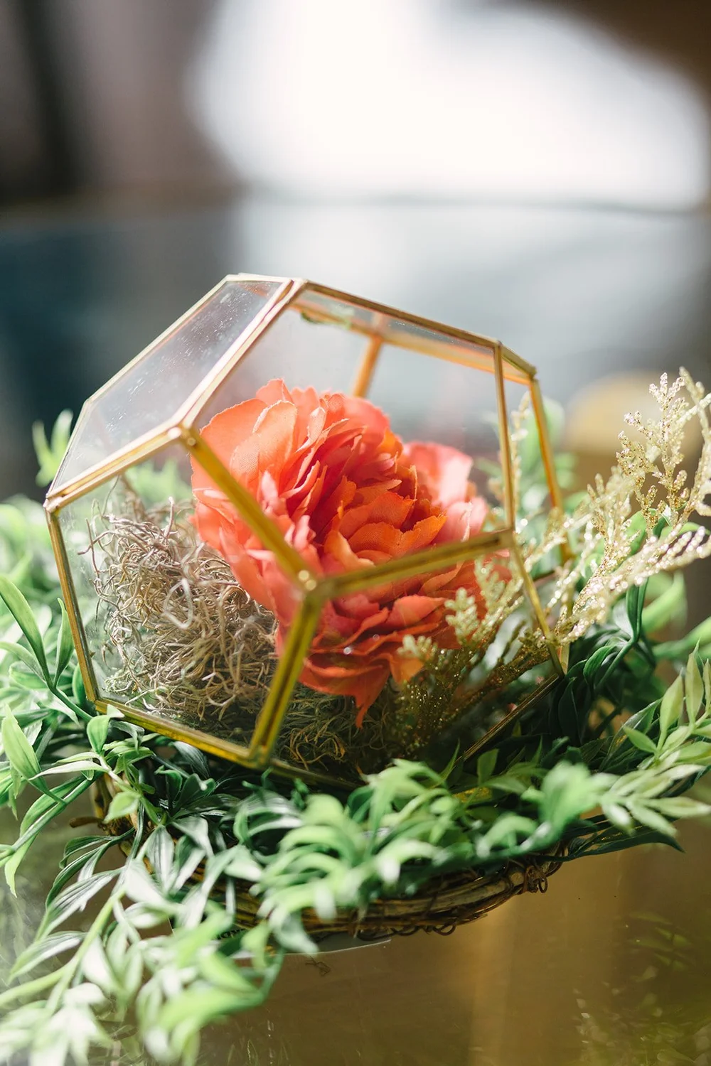 Gold geometric glass terrarium holding coral peonies and moss among greenery