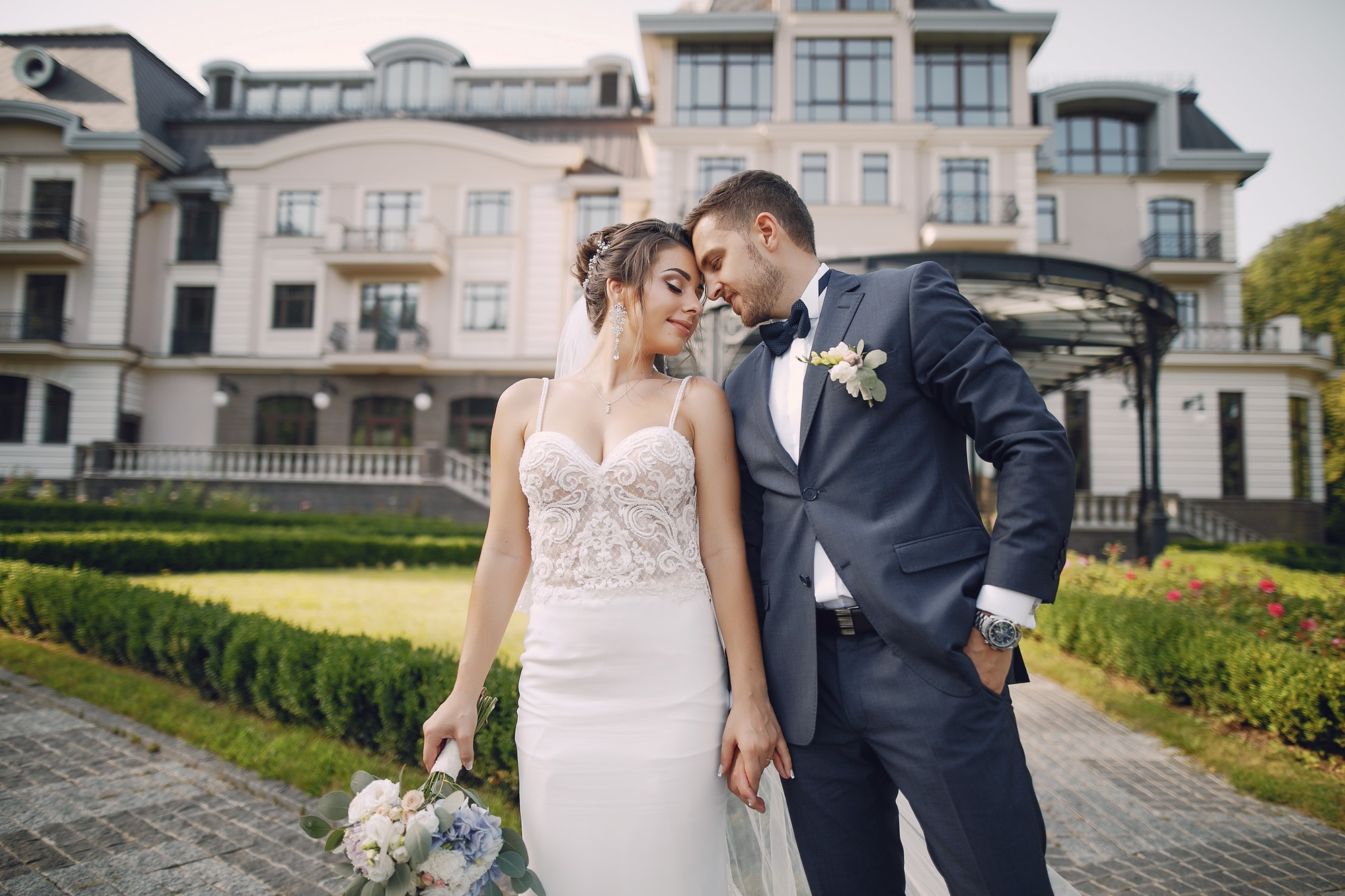 Bride and groom embracing on a manicured lawn in front of a grand stone building