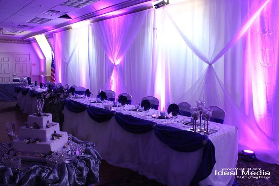 Head table in purple and lavender uplighting with white draping behind