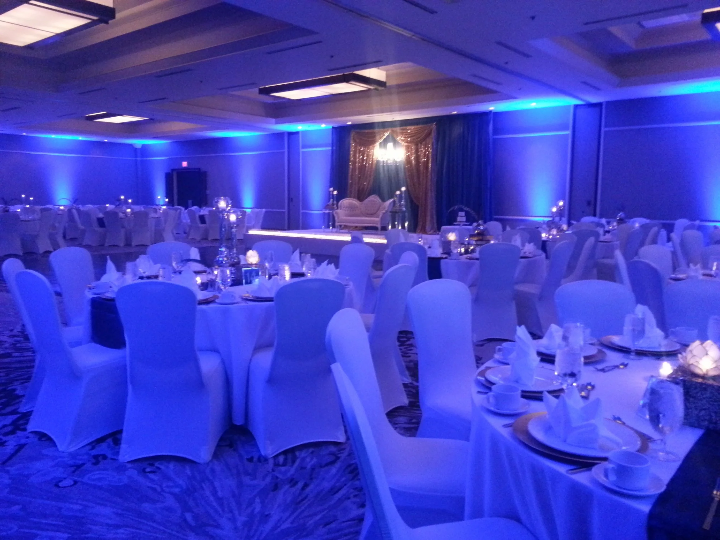 Hotel ballroom reception washed in deep blue uplighting with white chair covers