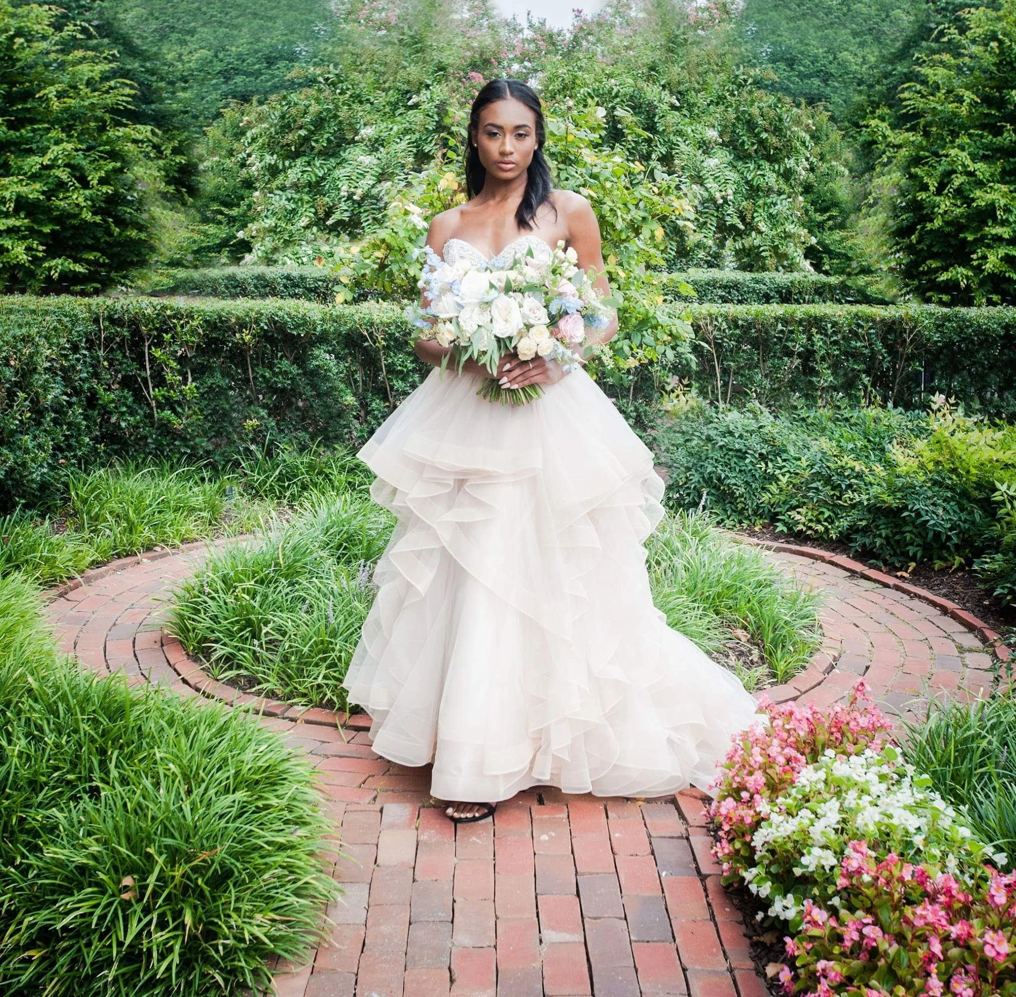 Bride in a ruffled ballgown holding a white bouquet on a garden path