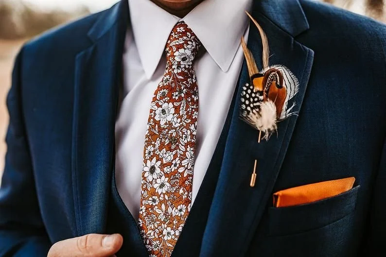 Navy suit with a rust floral tie and a feather boutonniere