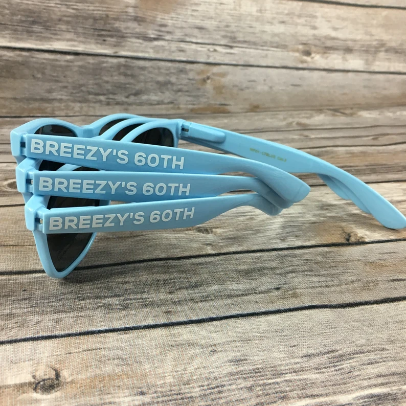 Pale blue heart shaped party sunglasses printed for a 60th birthday, laid on wood