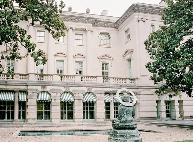 Neoclassical mansion facade with a fountain and manicured hedges
