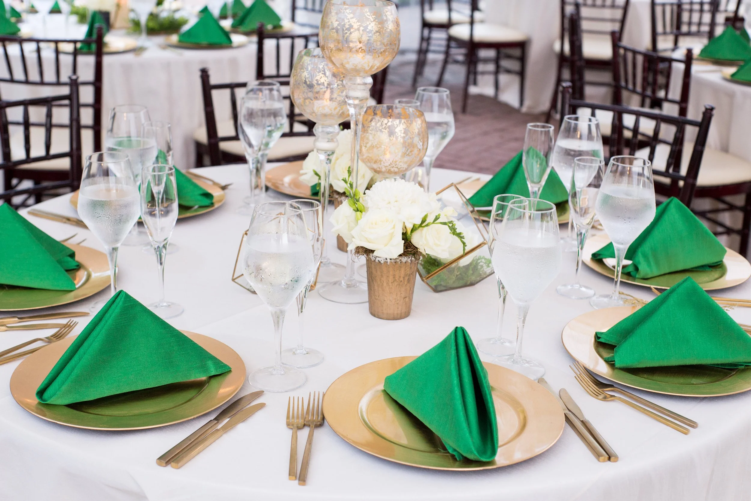 Reception place setting with emerald green napkins and gold chargers