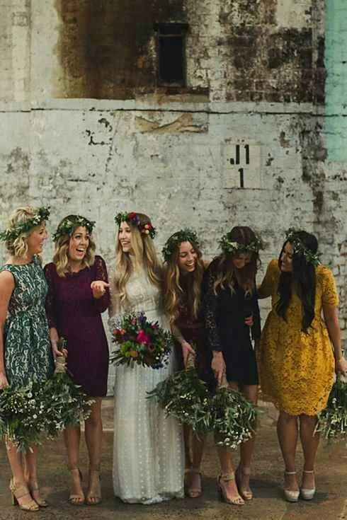 Bridesmaids in mixed jewel tone dresses laughing together against a brick wall