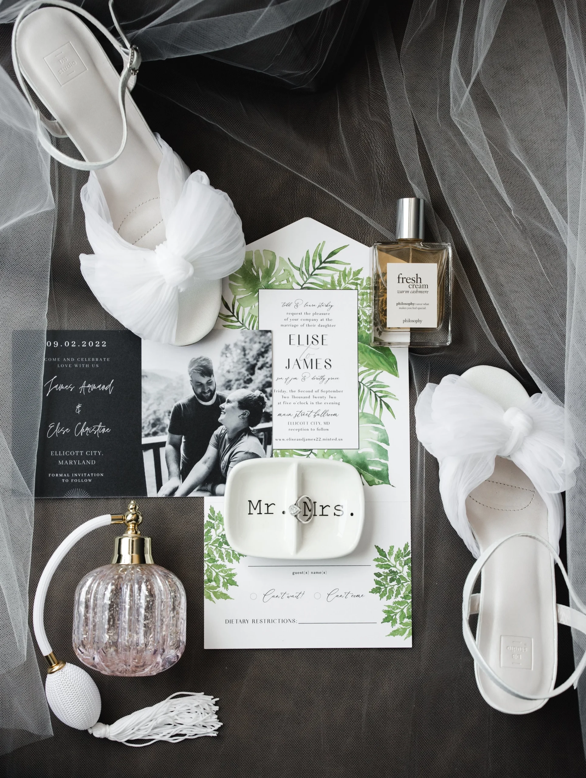 Flat lay of a black and white wedding invitation suite with perfume and hair pieces