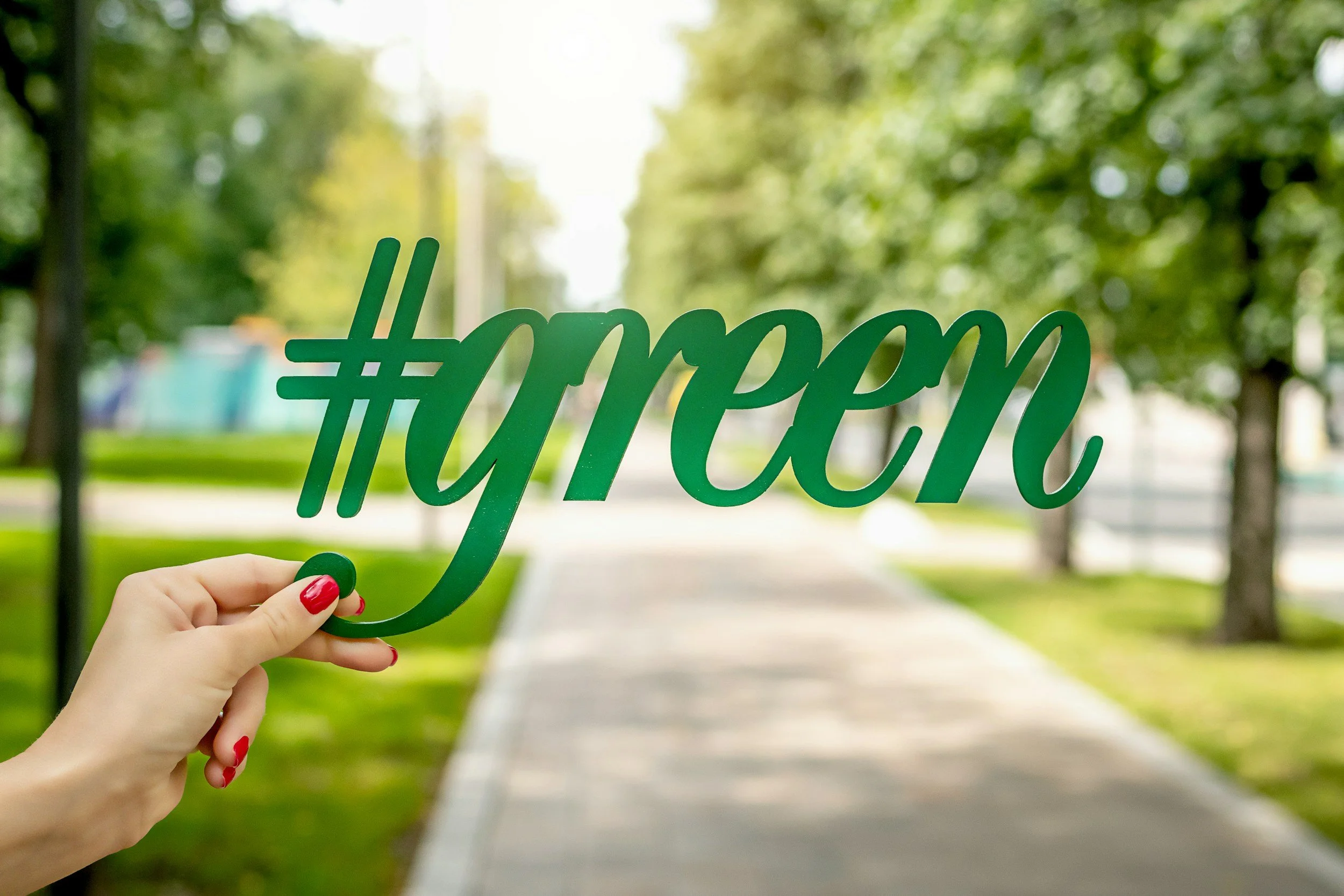 Hand holding a green hashtag green sign on a tree lined path