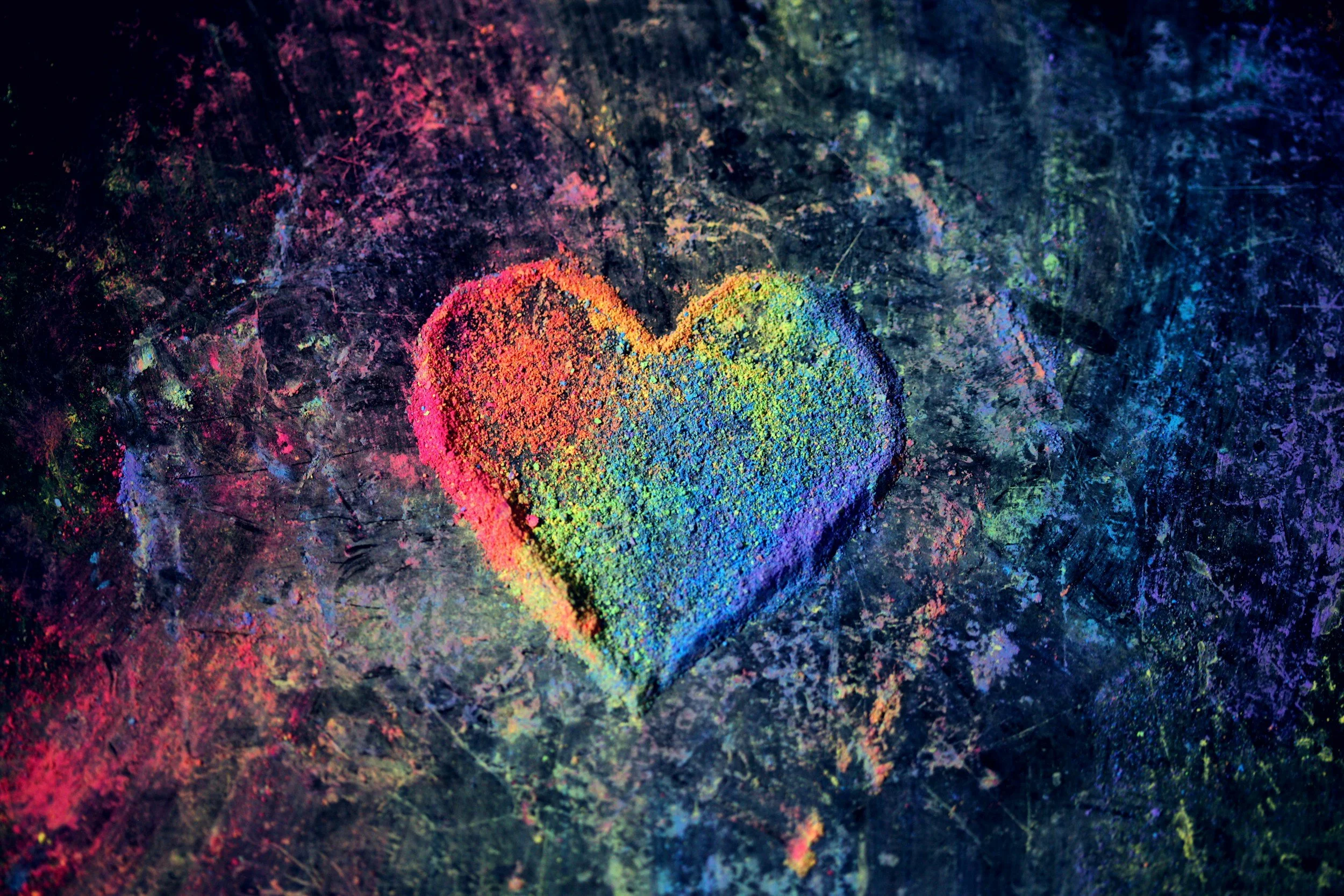 Heart shaped patch of rainbow coloured chalk powder on dark textured stone