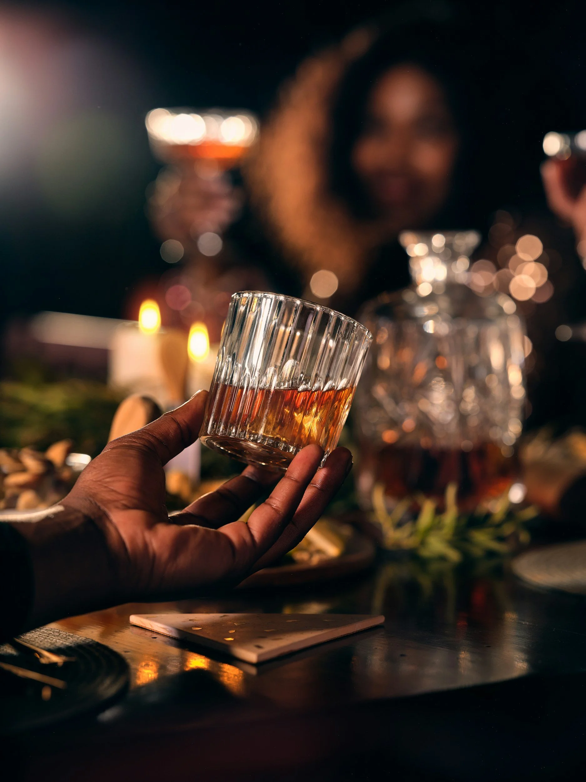 Hand holding a cut crystal glass of whiskey at a candlelit bar