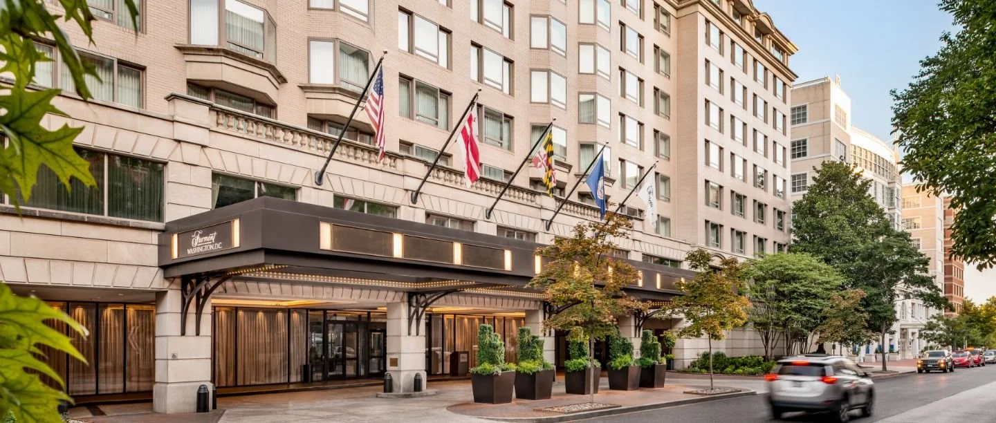 Entrance of a city hotel with flags and planters along the pavement