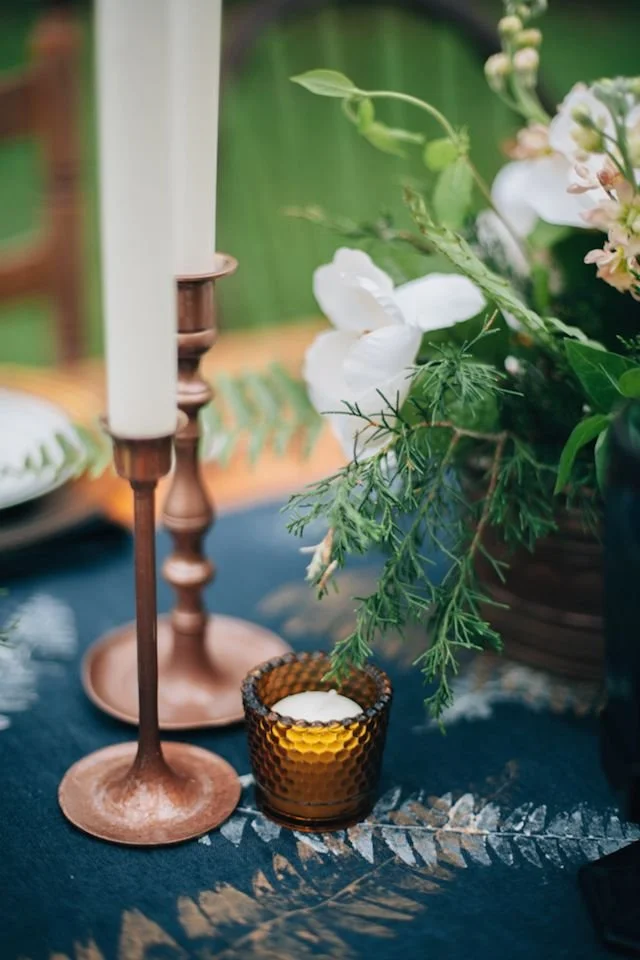 Table centrepiece with a taper candle, white orchid and greenery in soft candlelight