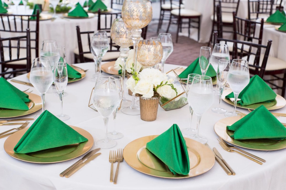 Reception tablescape with green napkins, gold chargers, and a floral runner